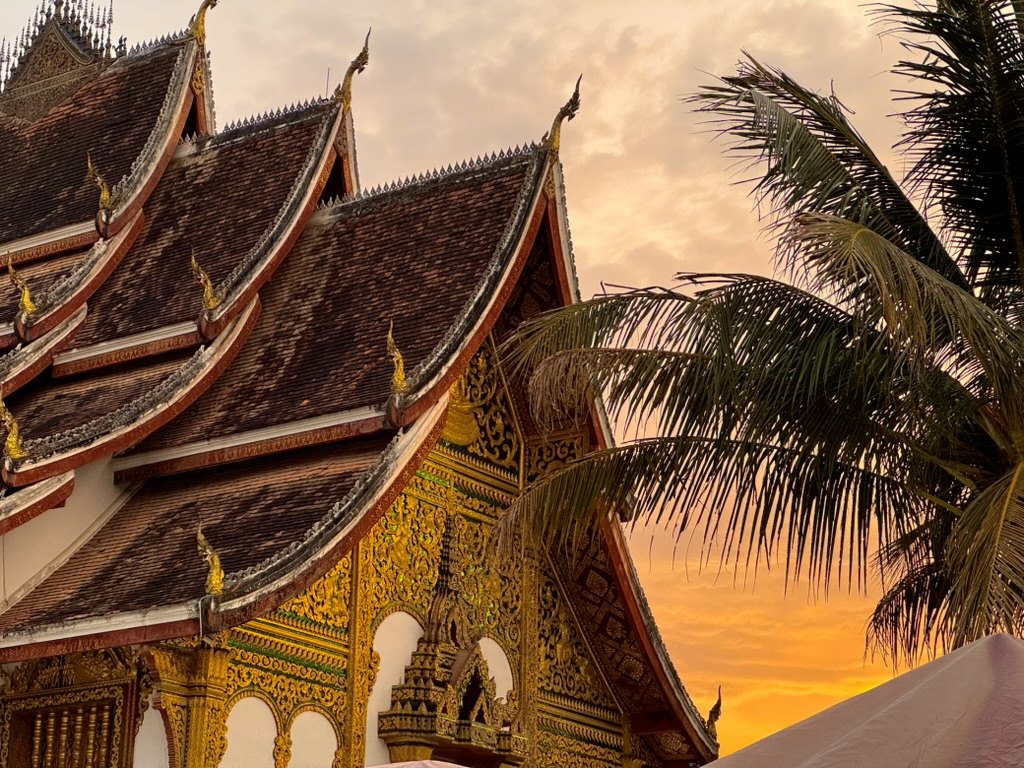 Temple traditionnel au Laos sous un ciel orangé au coucher du soleil
